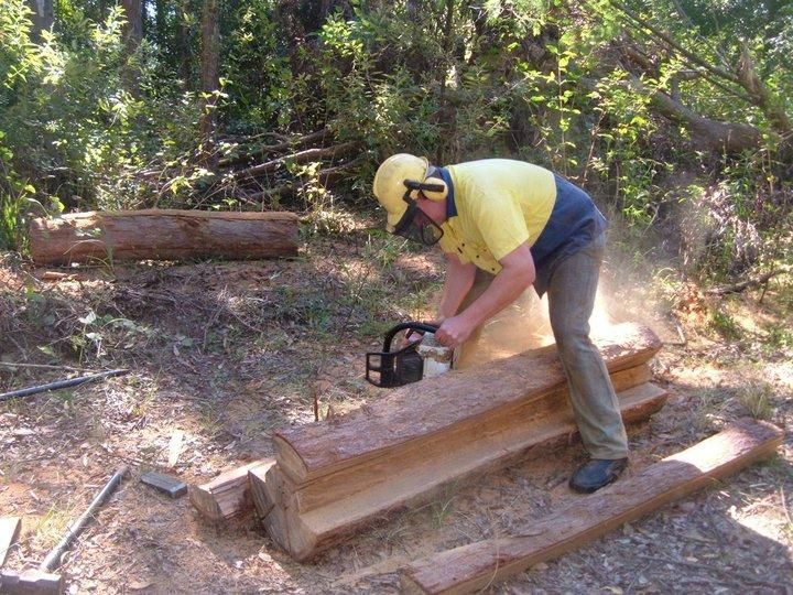 a Man is Cutting a Log With a Chainsaw — Tony Sinclair Fencing In Coffs Harbour, NSW