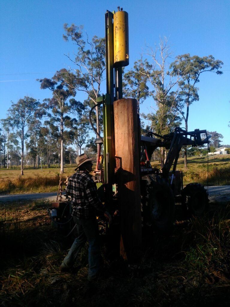 a Man in a Plaid Shirt is Working on a Machine in a Field — Tony Sinclair Fencing In Bucca, NSW
