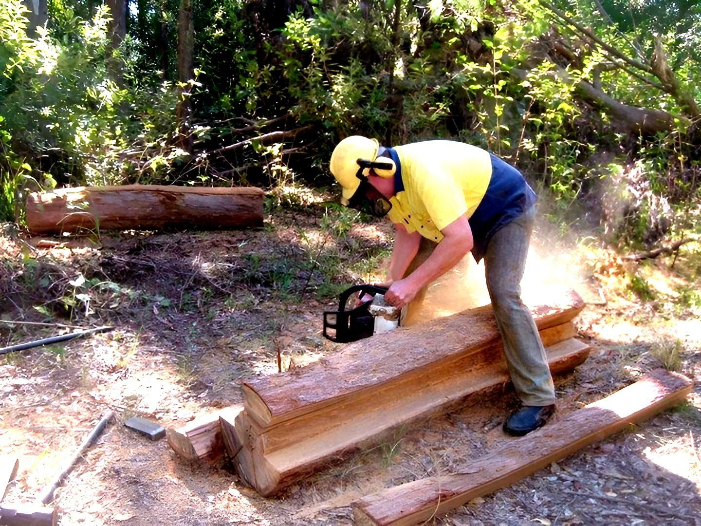 a Man is Using a Chainsaw to Cut a Log — Tony Sinclair Fencing In Bucca, NSW