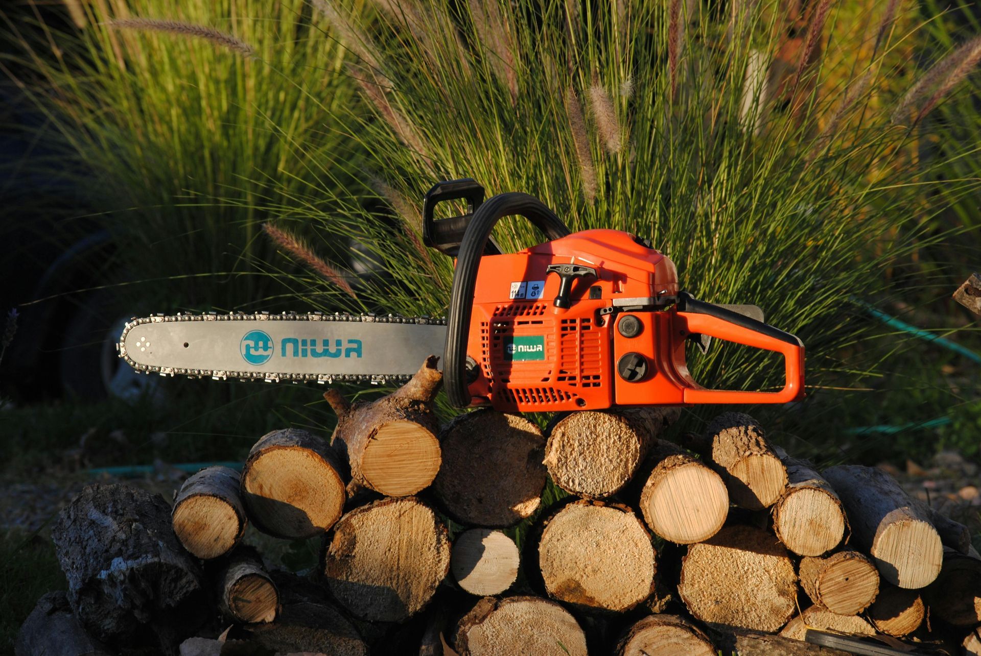 Orange Niwa chainsaw resting on a stack of cut logs outdoors.