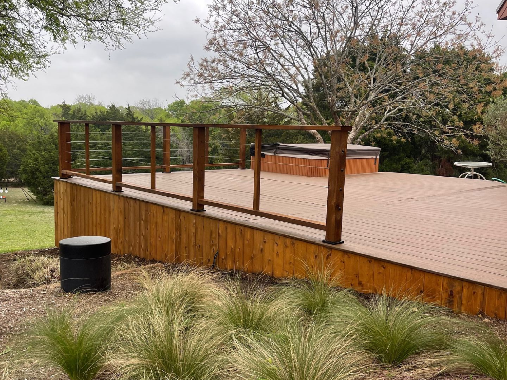 Wooden deck with railing, a hot tub, and surrounding greenery.