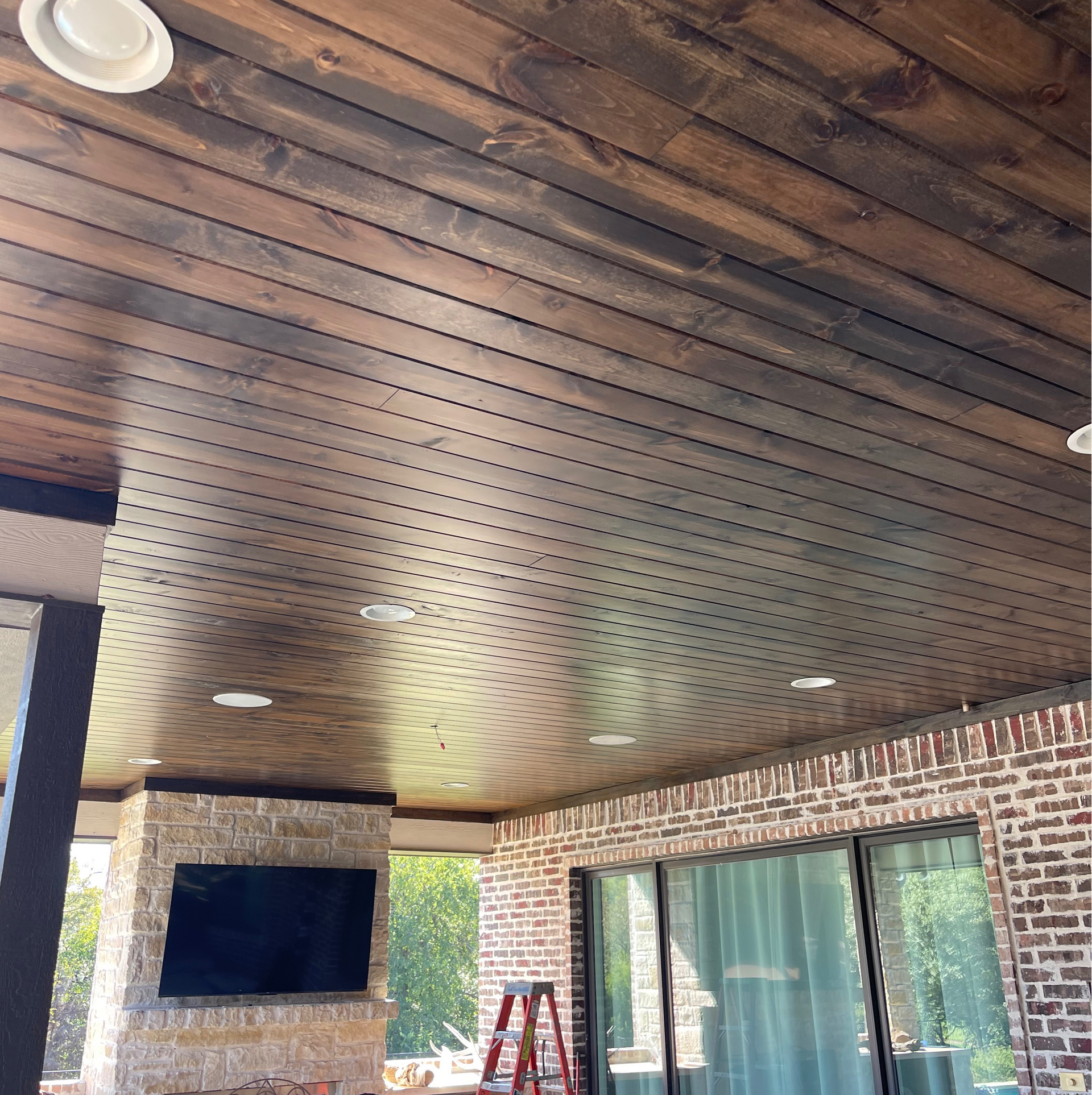 Dark stained wooden ceiling with recessed lights, above brick and stone outdoor space.