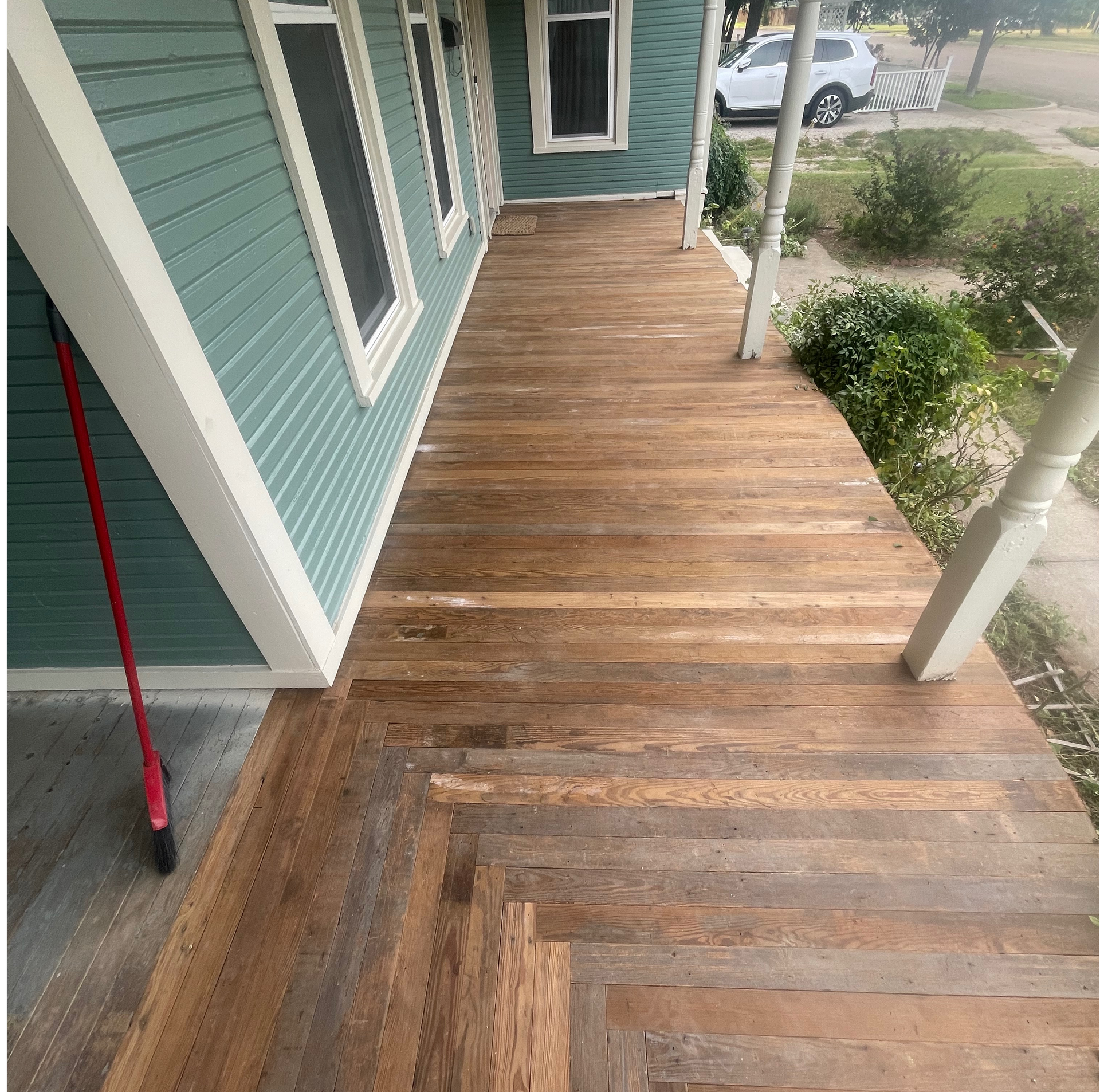 Wooden porch with teal siding and white trim. Broom leaning against the siding.