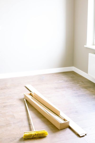 Broom and trim boards on wood floor of a room with white walls and a window.