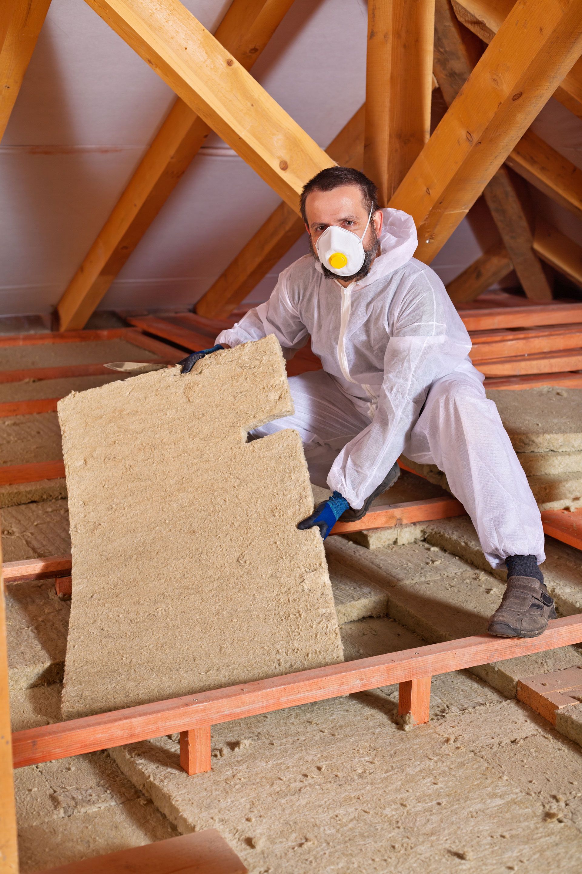 Man in protective suit installing insulation in attic.