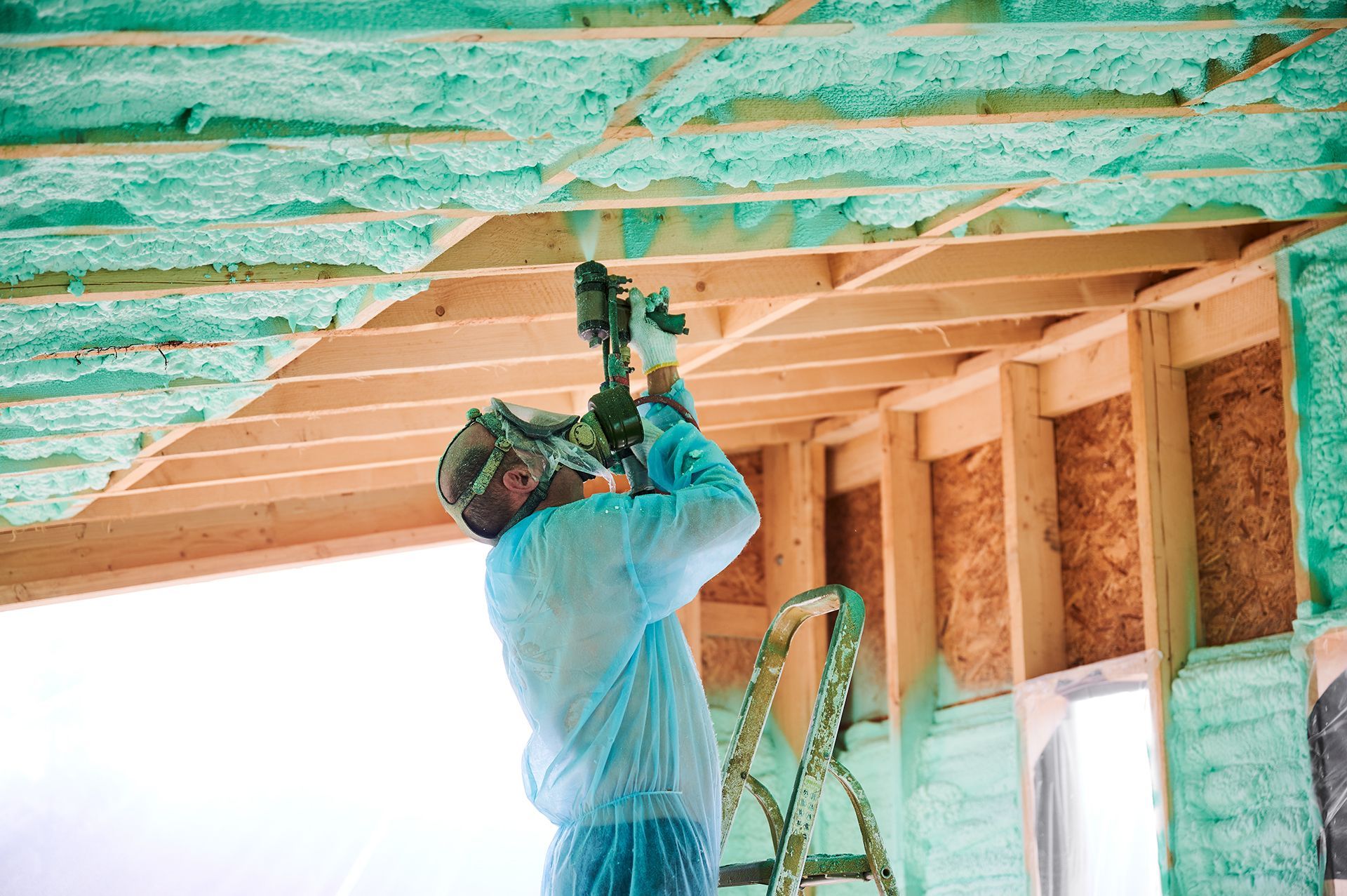 A man is spraying insulation on the ceiling of a house.
