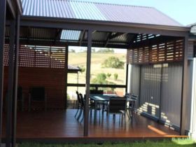 Covered outdoor wooden deck with a dining set, featuring lattice privacy screens and metal roofing overlooking a field.
