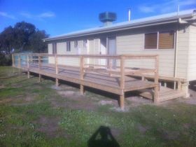 A long wooden accessibility ramp with handrails leading to the entrance of a light-colored building in a grassy field.