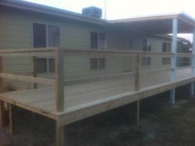 A long, light-colored wooden deck with a matching railing attached to the side of a house with pale siding.