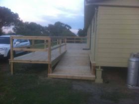 A wooden wheelchair ramp leading up to the entrance of a light-yellow house at dusk.
