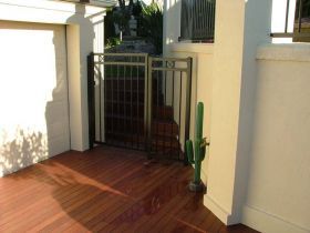 A metal gate separates a wooden deck from a set of stairs, with a decorative metal cactus placed beside the gate.