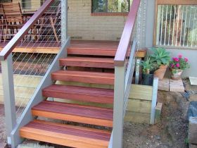 Wooden steps with red-brown treads and gray railings leading up to a patio deck with potted plants.
