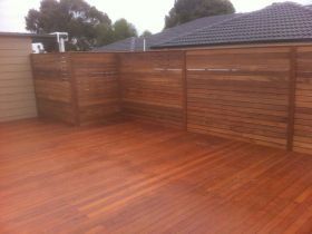 A clean, newly stained wooden deck with a matching horizontal-slat privacy fence in a backyard setting.