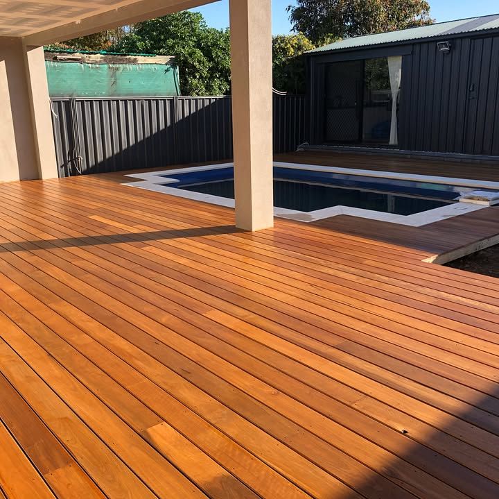 A swimming pool beside a polished wooden deck with two large decorative urns and a lounge chair.