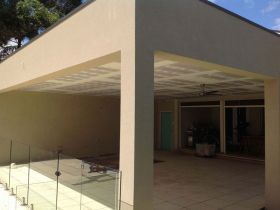 A modern cream-colored patio cover with a coffered ceiling and a glass railing overlooking a paved outdoor seating area.