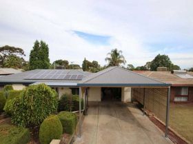 A suburban home with a dark grey metal carport, a driveway, and solar panels on the roof under a partly cloudy sky.