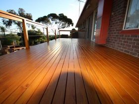 A freshly stained, polished wooden deck outside a brick house at sunset, featuring a wooden railing and a scenic view.