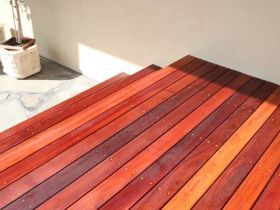 A high-angle view of wooden deck steps leading to a light-colored wall with a potted plant on the left.