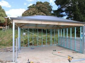 An outdoor timber and steel frame structure with a grey corrugated metal roof, currently under construction on concrete.