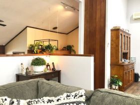 A living area showing a couch in the foreground, a low divider wall with plants, and a wooden hutch on the right.