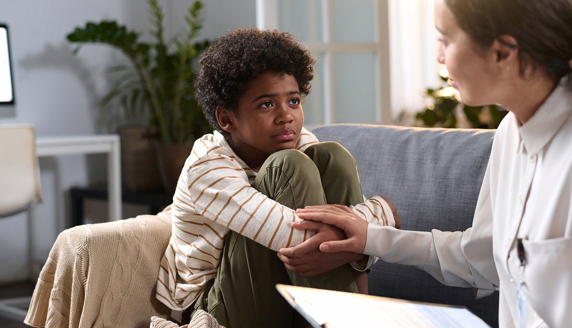 Boy with concerned expression being comforted by person on a couch.