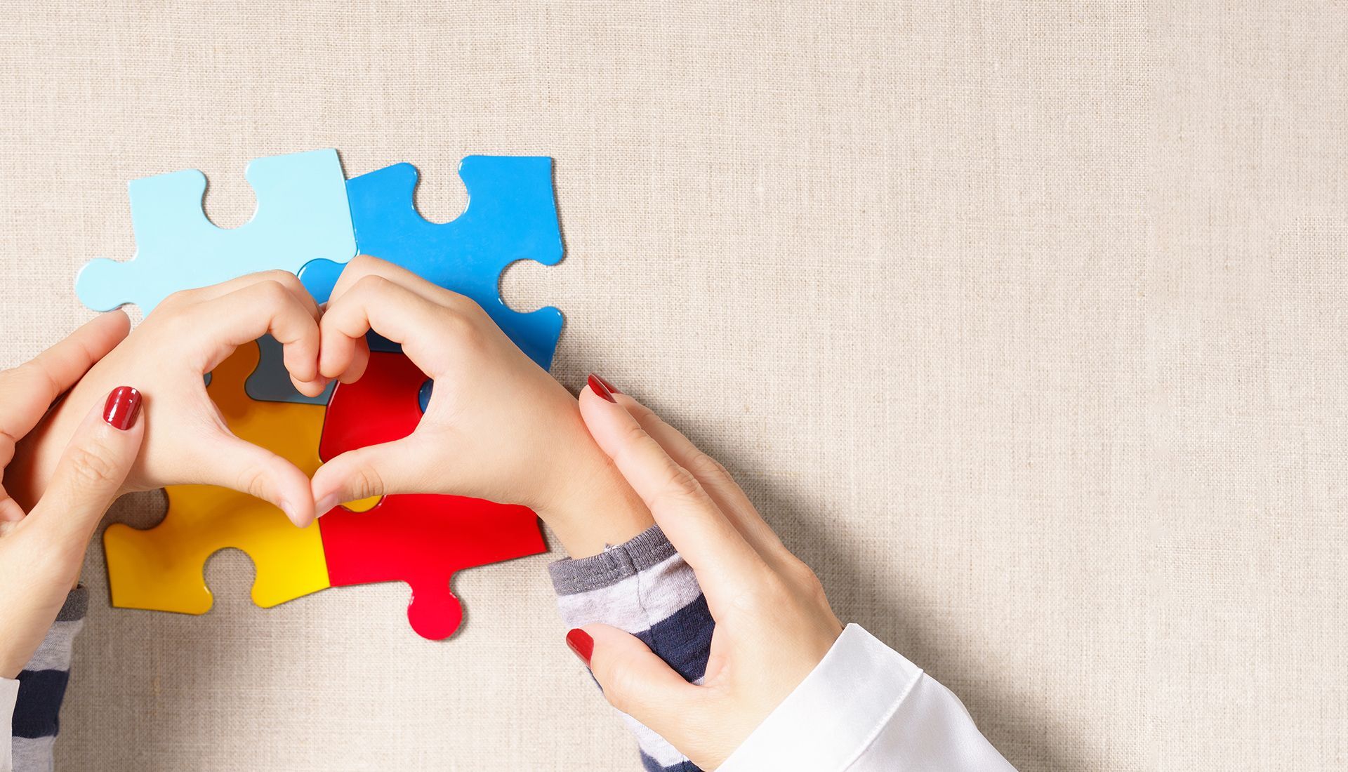 Hands forming a heart over puzzle pieces in blue, yellow, and red.