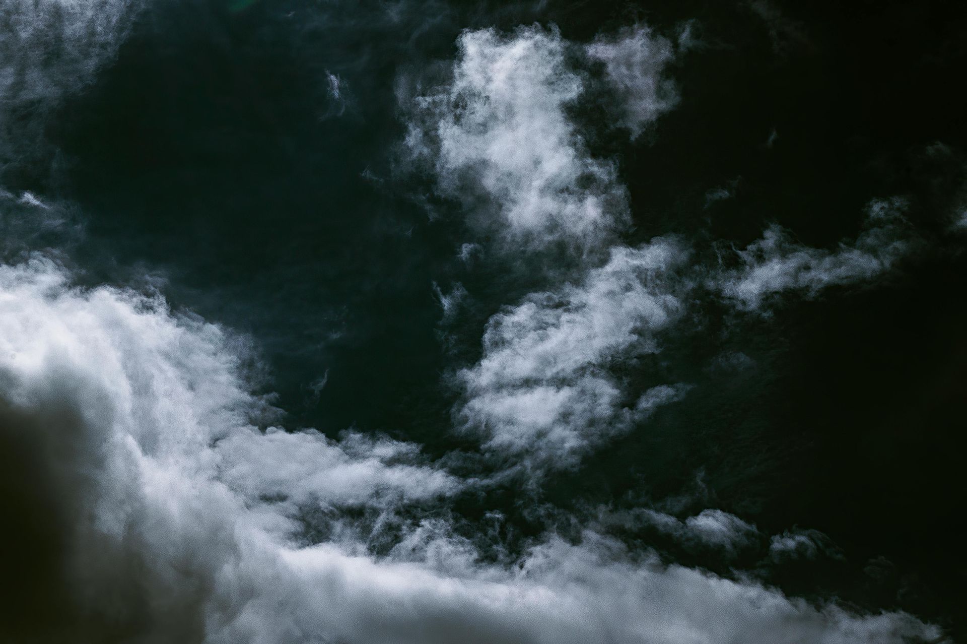 Wispy white clouds drift against a deep, dark, and moody sky.