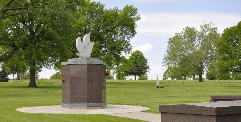 There is a statue of a dove in the middle of a cemetery.