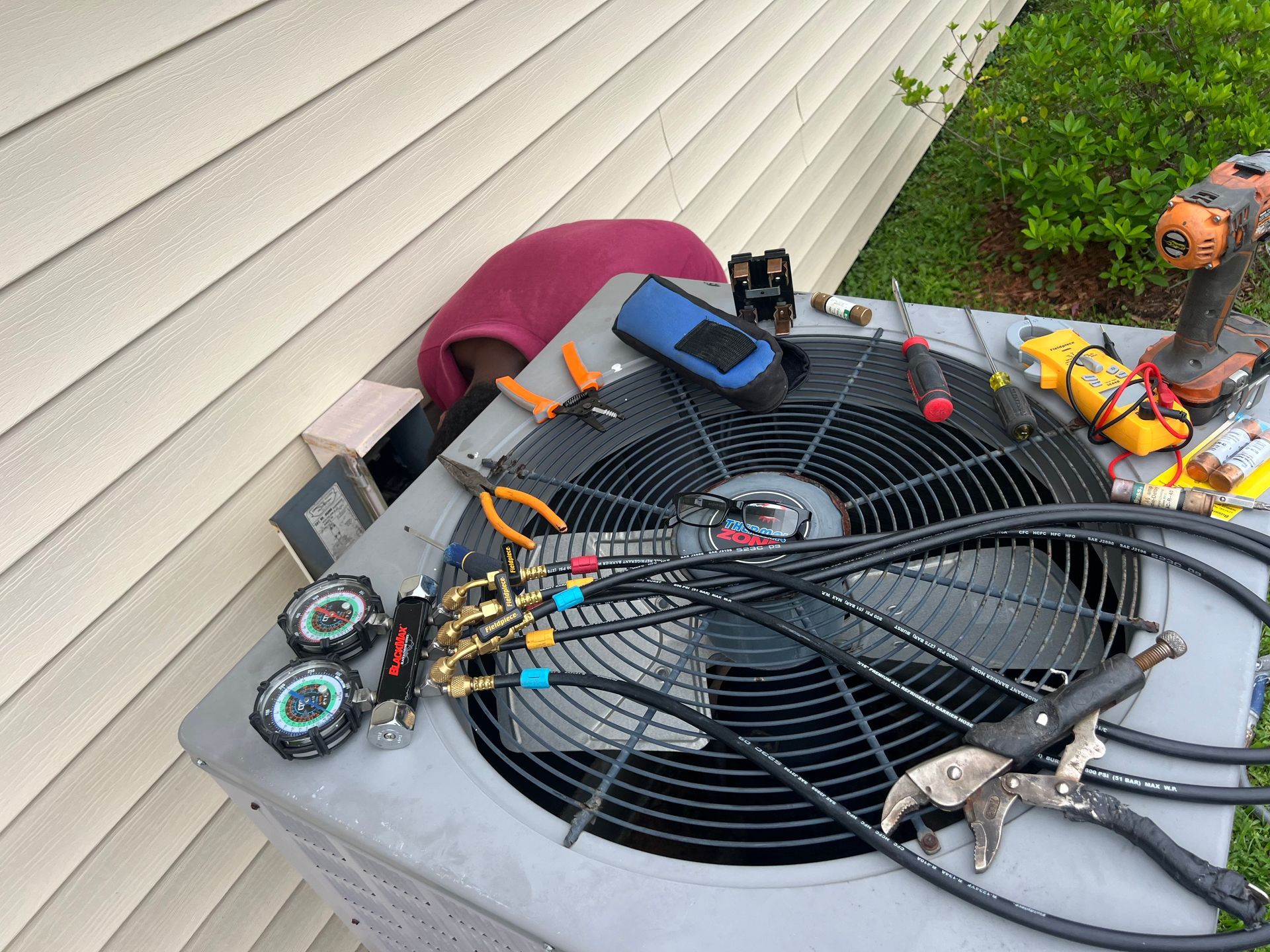 HVAC technician repairing an air conditioner unit outdoors, tools and gauges visible.