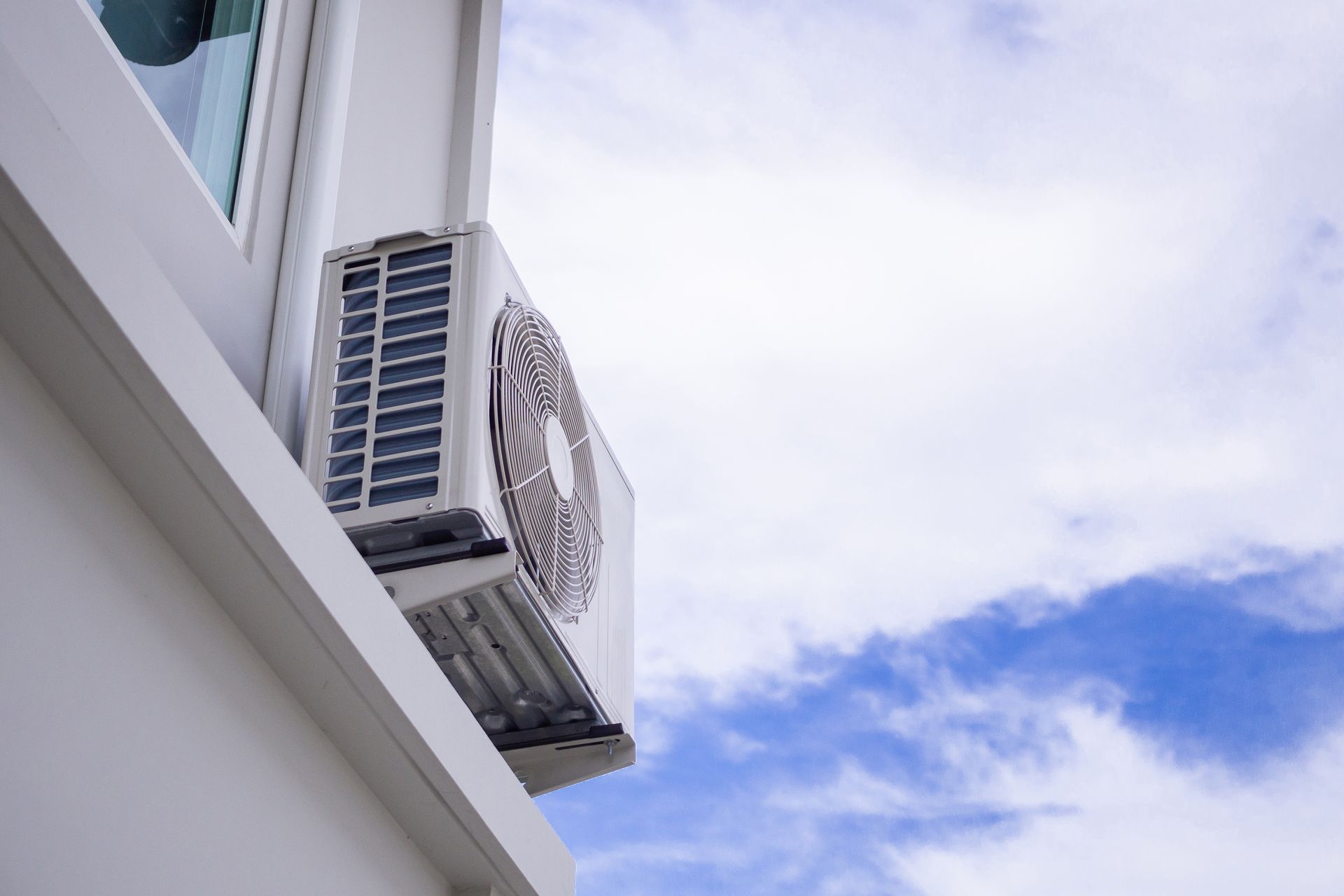 White air conditioning unit mounted on a white building exterior, with a blue sky background.