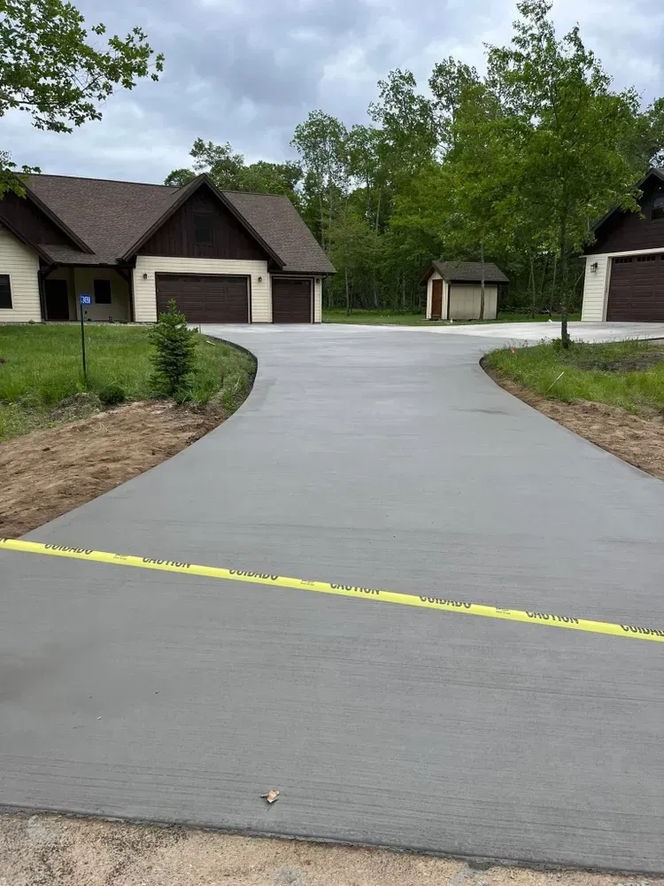 Newly poured concrete driveway curves toward a house with two attached garages under a cloudy sky.