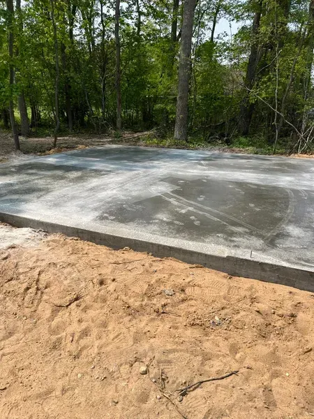 A freshly poured concrete pad with a sand border, trees in the background.