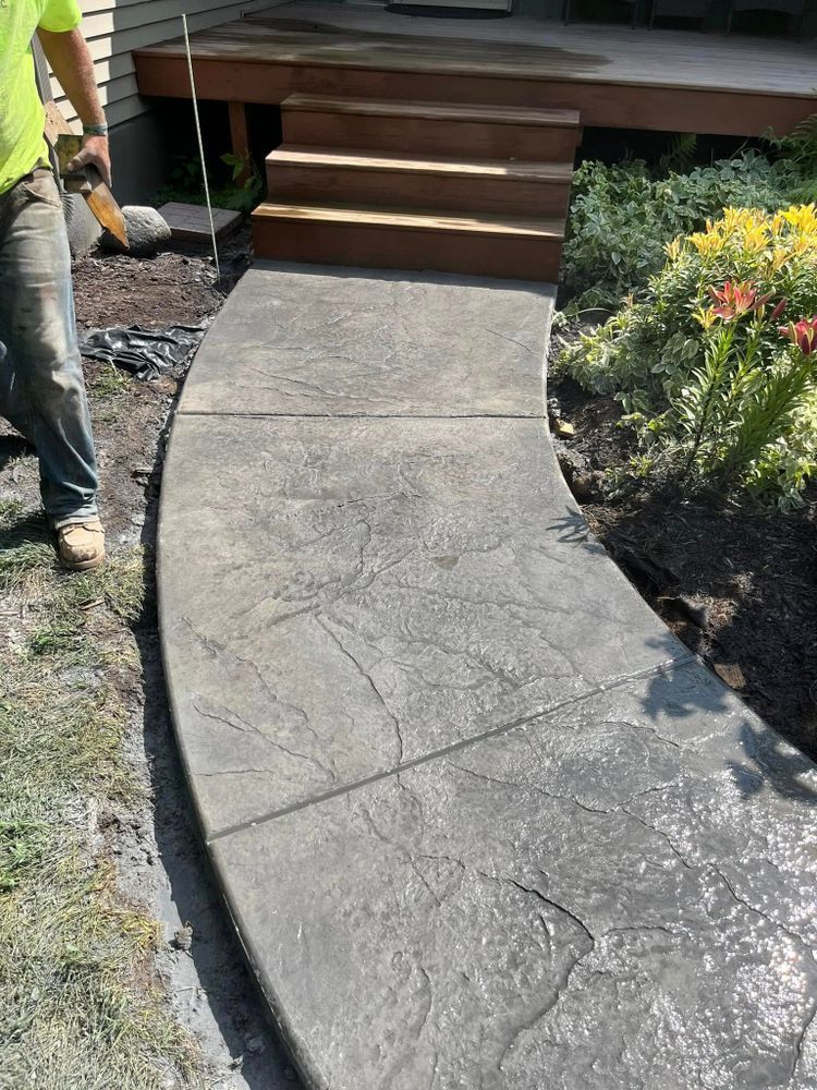 A concrete walkway with a leaf pattern, leading to wooden steps and a deck. A worker stands nearby.