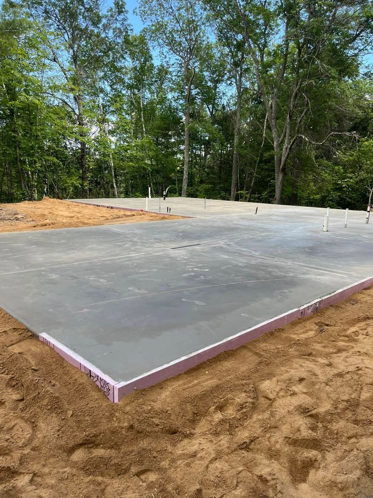 Concrete foundation with pink foam edge in a sandy, wooded area.