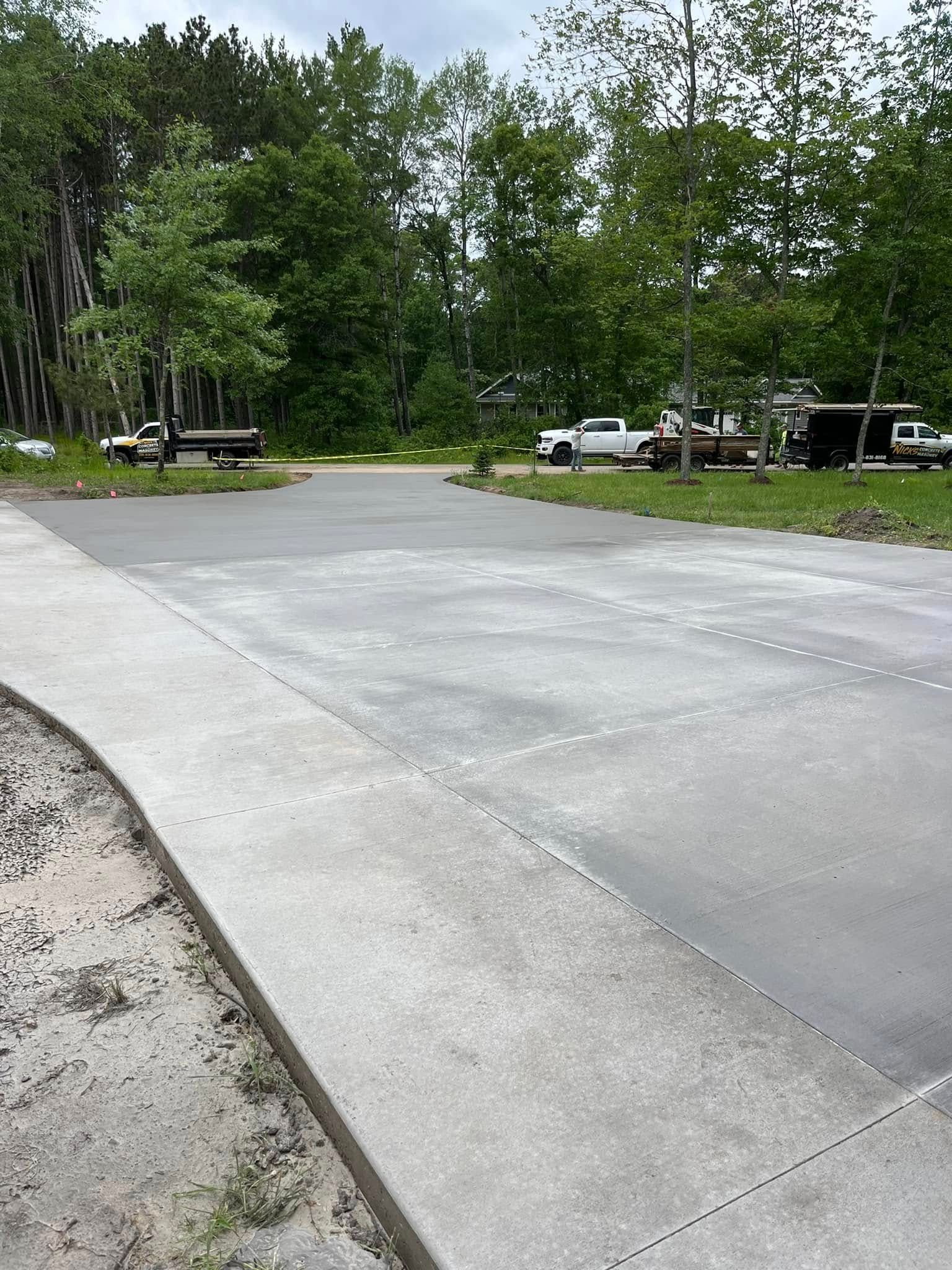 A large concrete surface with cut grooves; trees and parked vehicles are in the background.