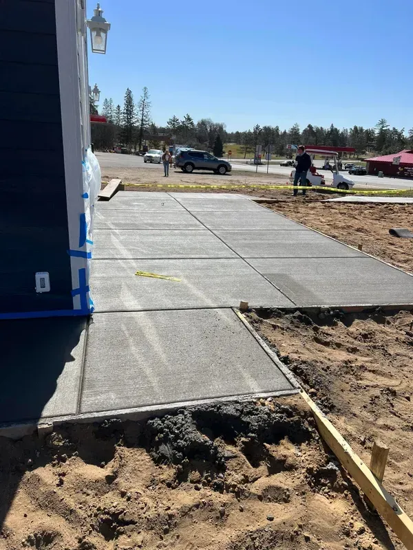 Concrete walkway being constructed next to a blue building on a sunny day.