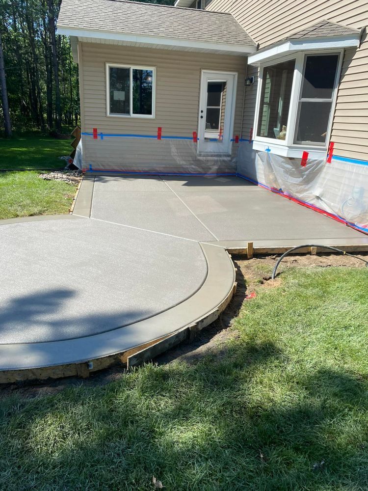 Newly poured concrete patio next to a house with a curved edge and small retaining wall.