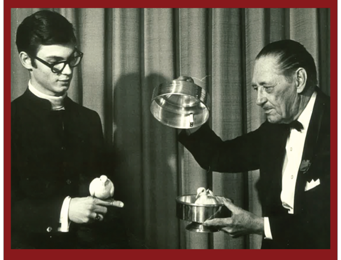 A black and white photo of a man in a tuxedo holding a bowl