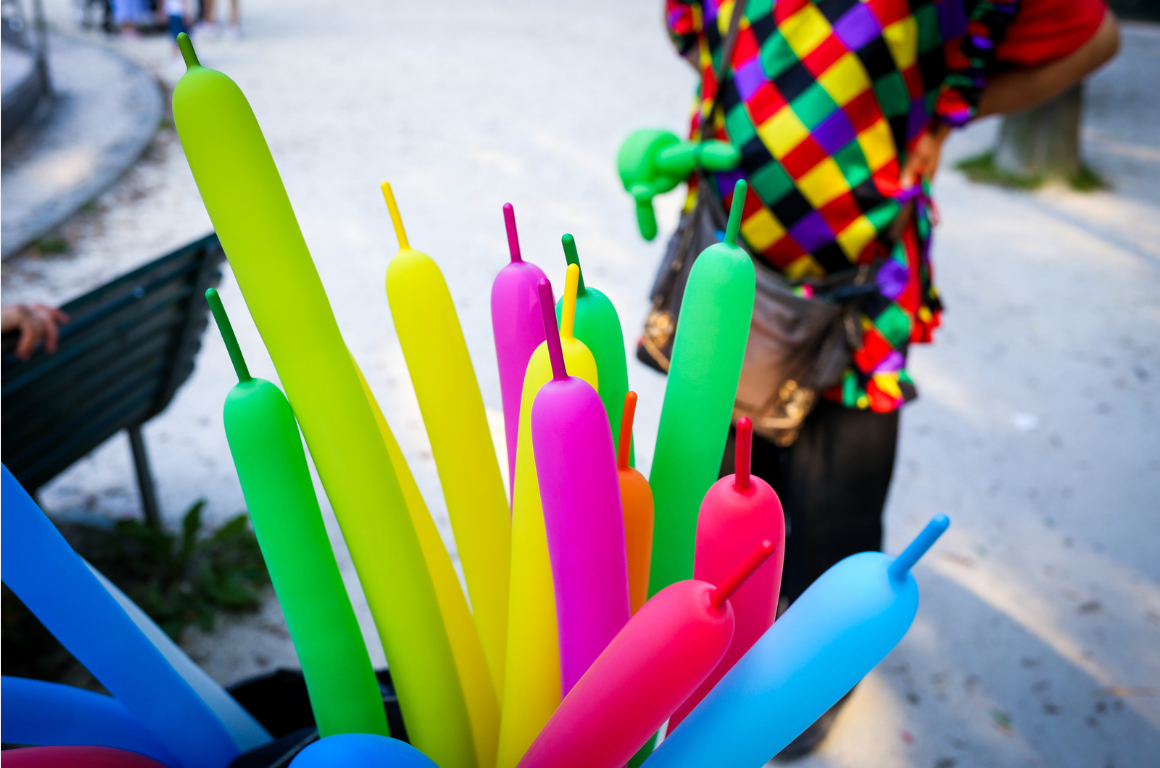 A person in a clown costume is holding a bunch of colorful balloons.