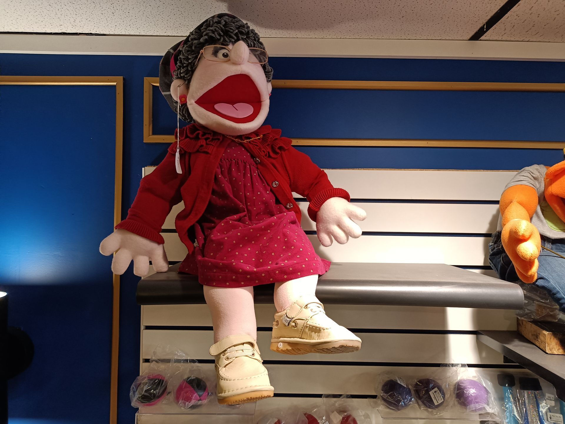A puppet in a red dress is sitting on a shelf