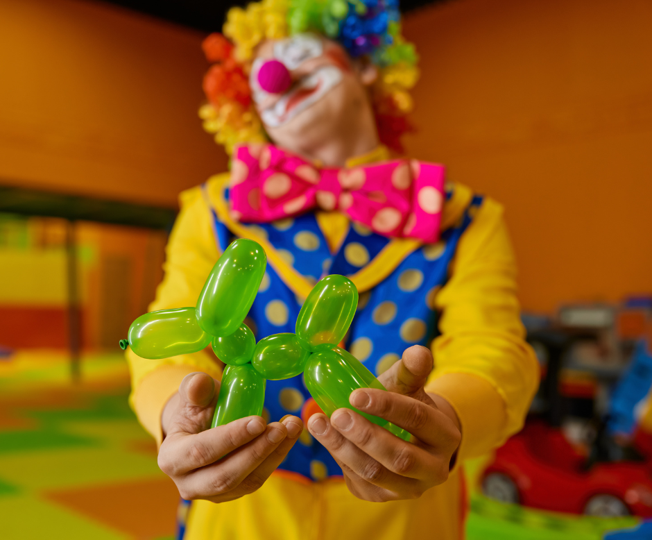 A clown is holding two green balloons in his hands.