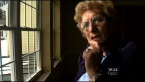 An elderly woman is sitting in front of a window looking out.