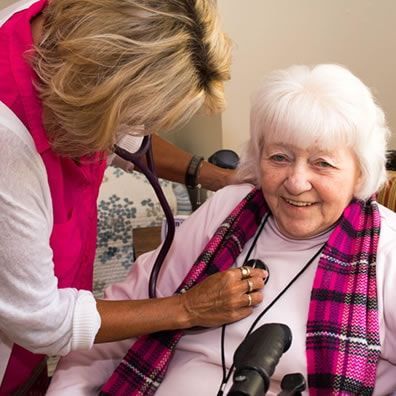 A woman is listening to an elderly woman 's heartbeat with a stethoscope