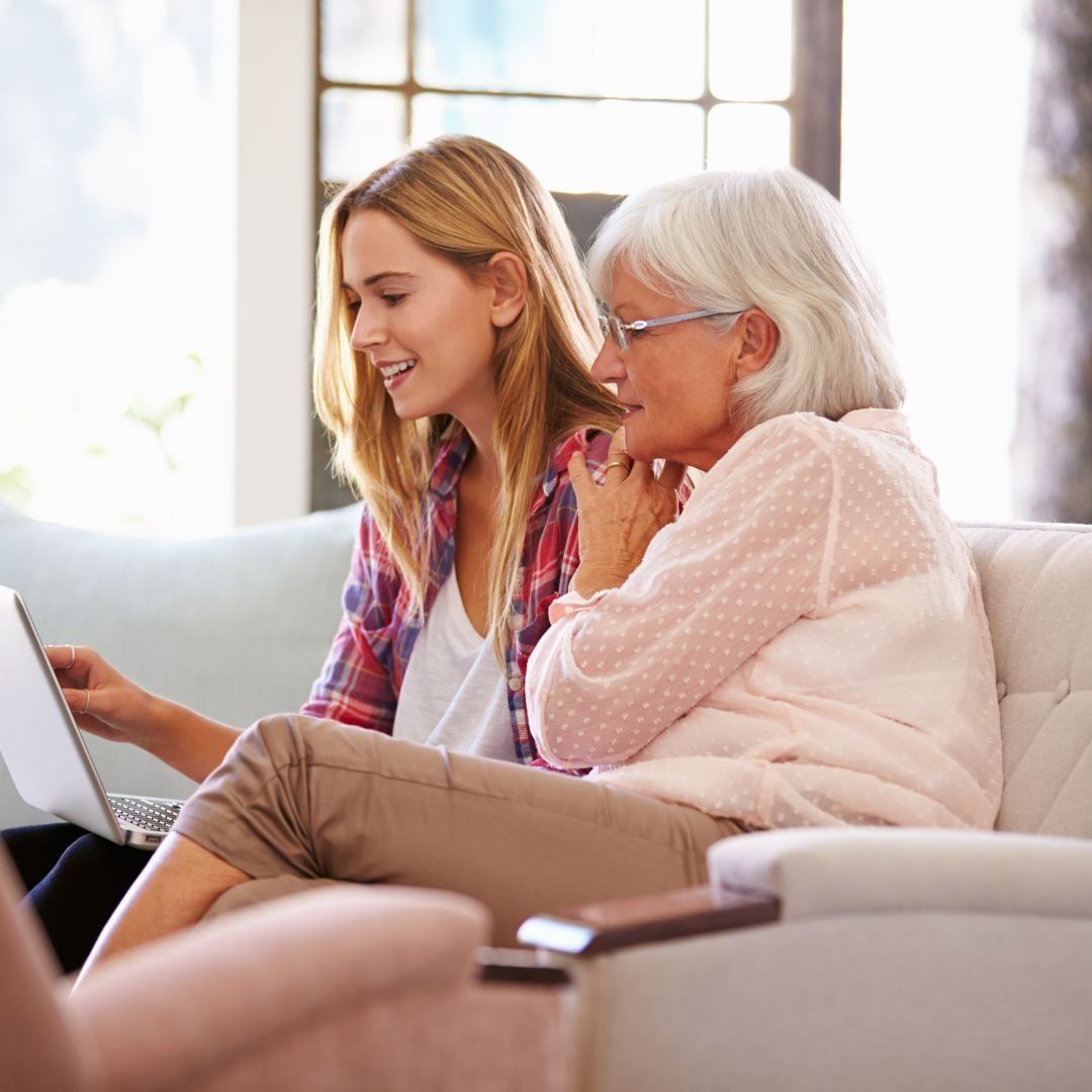 Two women are sitting on a couch looking at a laptop