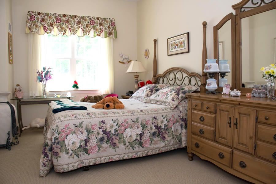 A bedroom with a bed , dresser , mirror and window.