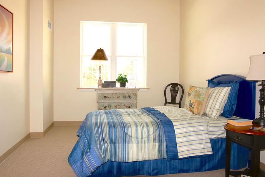 A bedroom with a bed , nightstand , lamp and window.