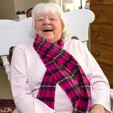 An elderly woman wearing a pink scarf is sitting in a rocking chair