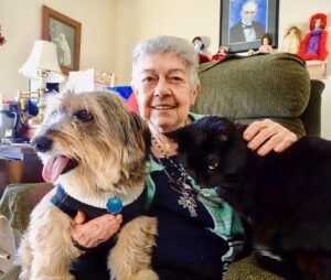 An elderly woman is sitting in a chair with two dogs.