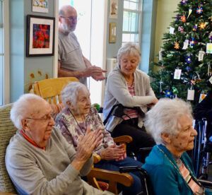 A group of elderly people are sitting in chairs in front of a christmas tree.