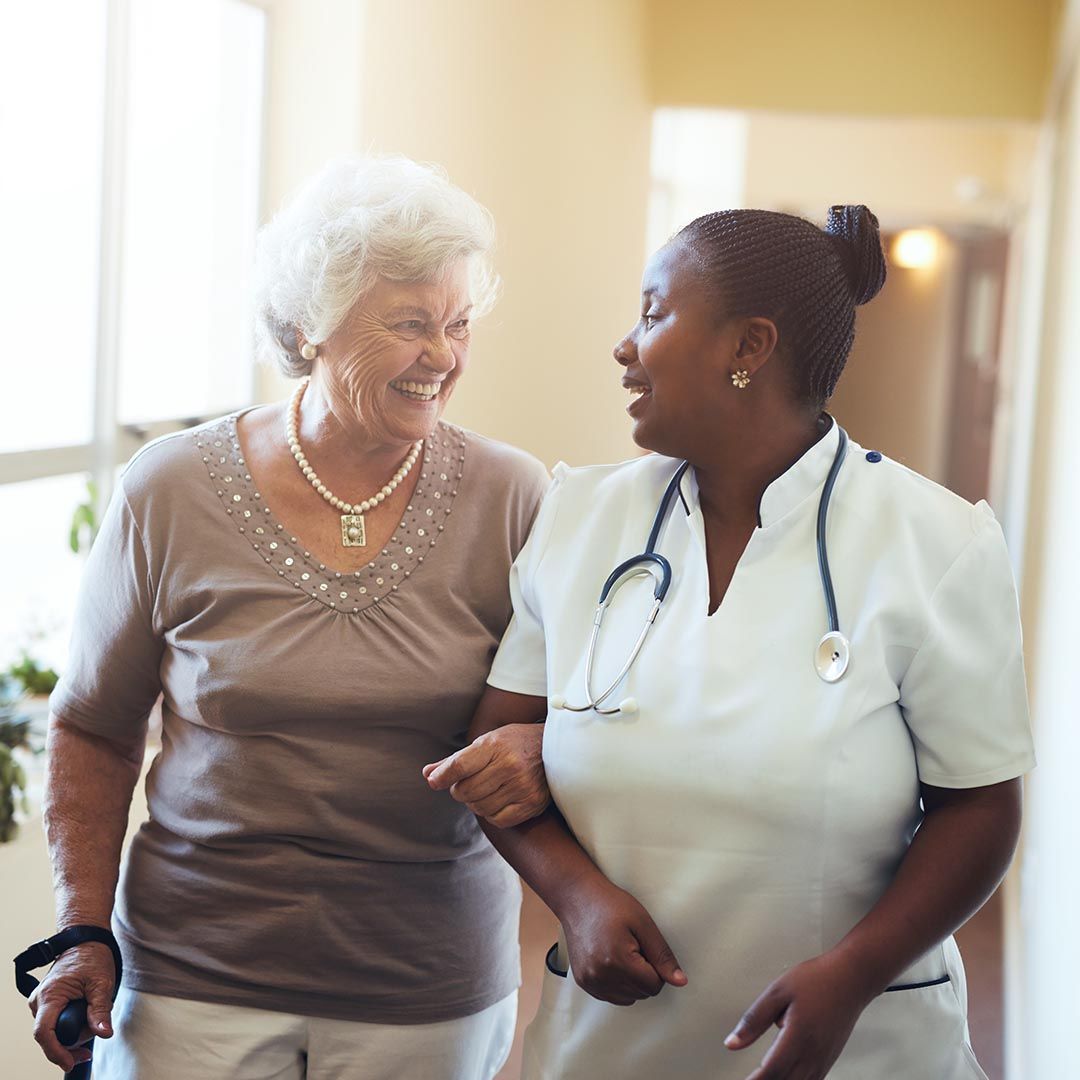 Nurse assisting senior woman walking down a hallway